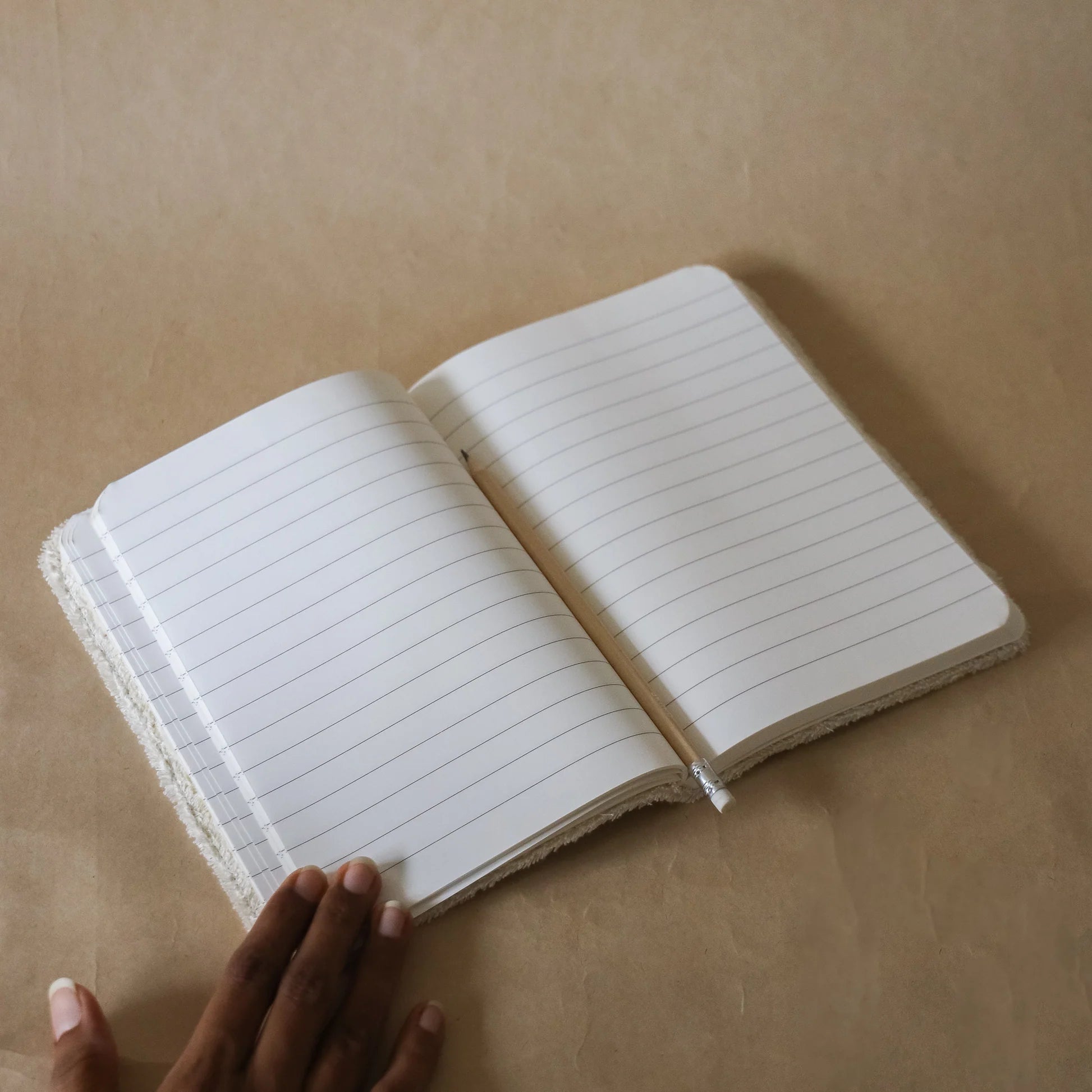 Open Akiiko journal with lined pages on a beige surface, held by a hand.