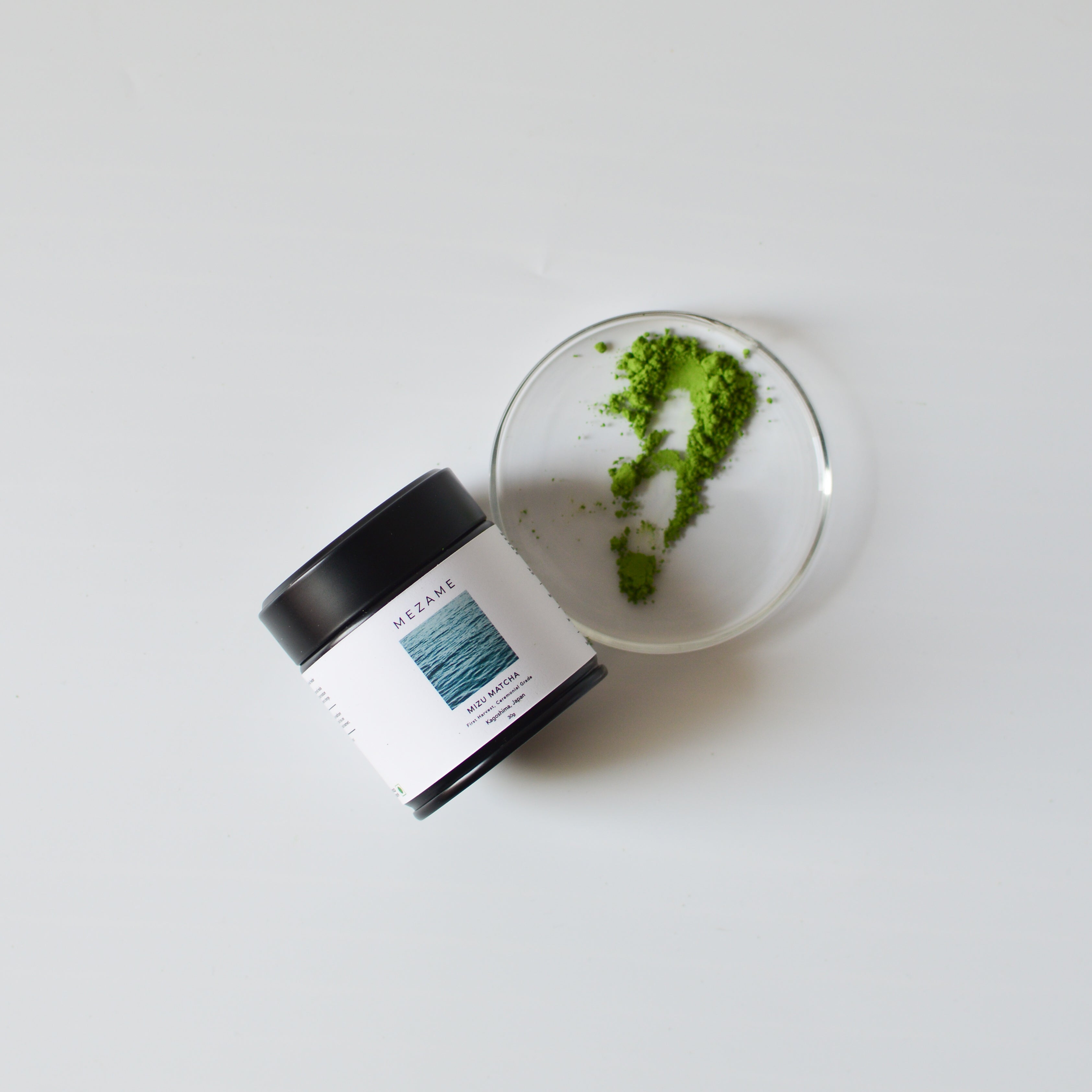 Vibrant green matcha powder with a black tin of ceremonial matcha on a white background