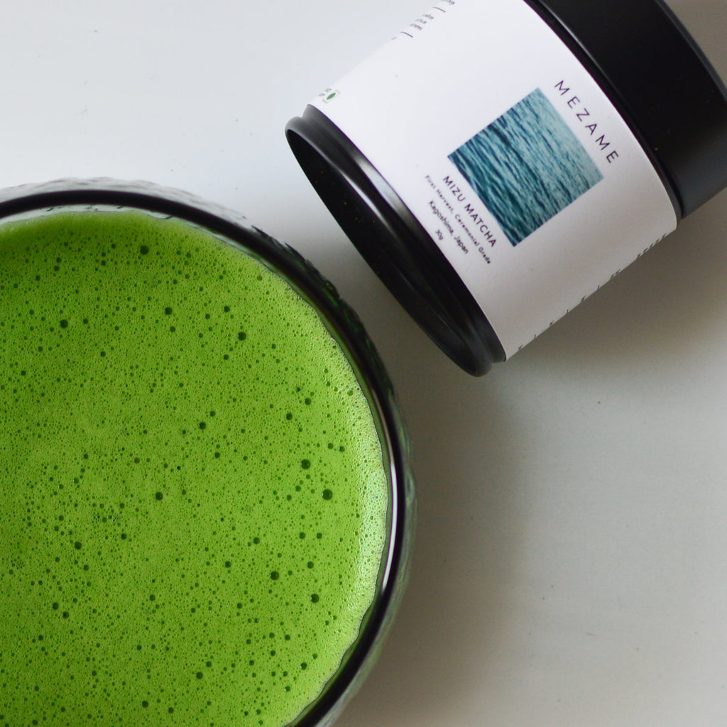 Green matcha tea in a glass with a container labeled 'MEZAME' on a white background