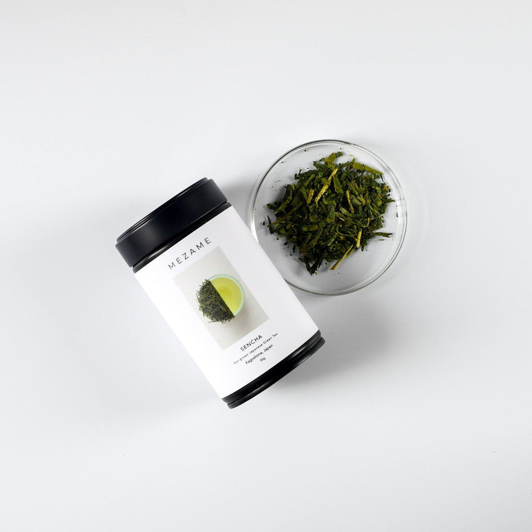 Sencha green tea packaging with a glass container of green tea leaves on a white background