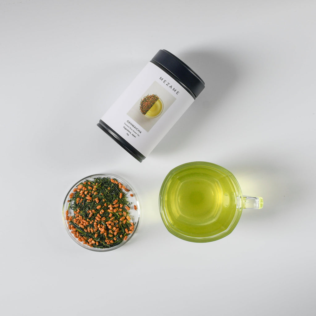 Mezame genmaicha green tea packaging with a transparent container of genmiacha tea leaves on a light gray background