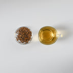 Tea cup with brewed Japanese hojicha tea and loose hojicha roasted green tea leaves on a white background