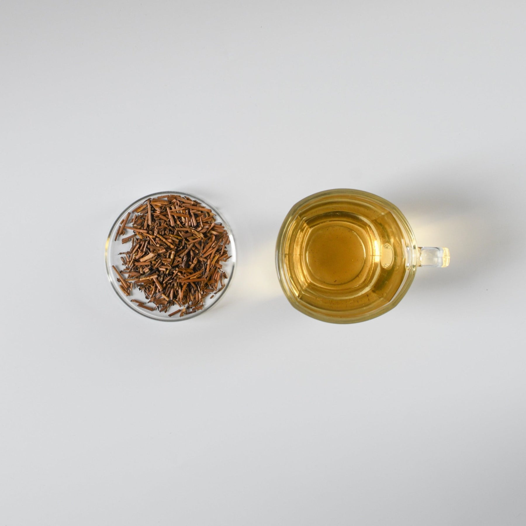 Tea cup with brewed Japanese hojicha tea and loose hojicha roasted green tea leaves on a white background