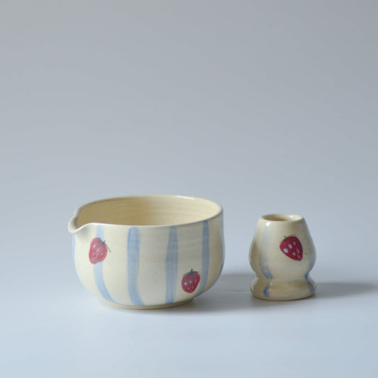 Ceramic chawan matcha bowl and chasen whisk holder with a strawberry design on a light gray background