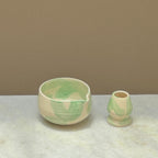 Ceramic matcha bowl and bamboo whisk holder with green and white marbled pattern on a neutral background