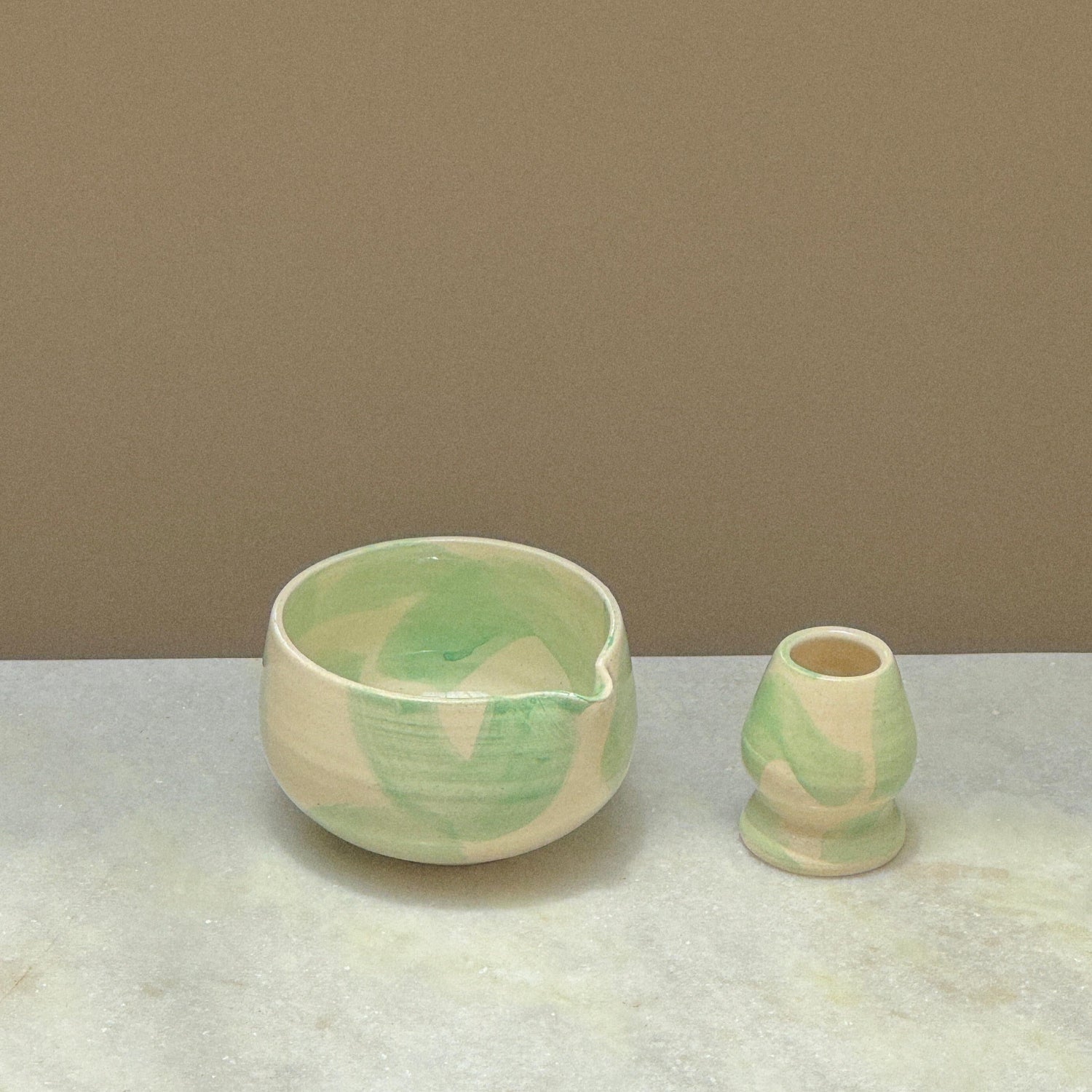 Ceramic matcha bowl and bamboo whisk holder with green and white marbled pattern on a neutral background