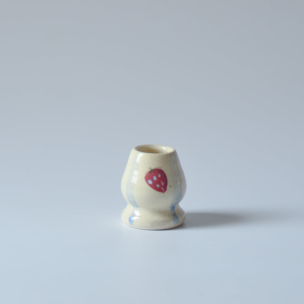Small ceramic chasen whisk holder with a red strawberry and blue stripes design on a light gray background