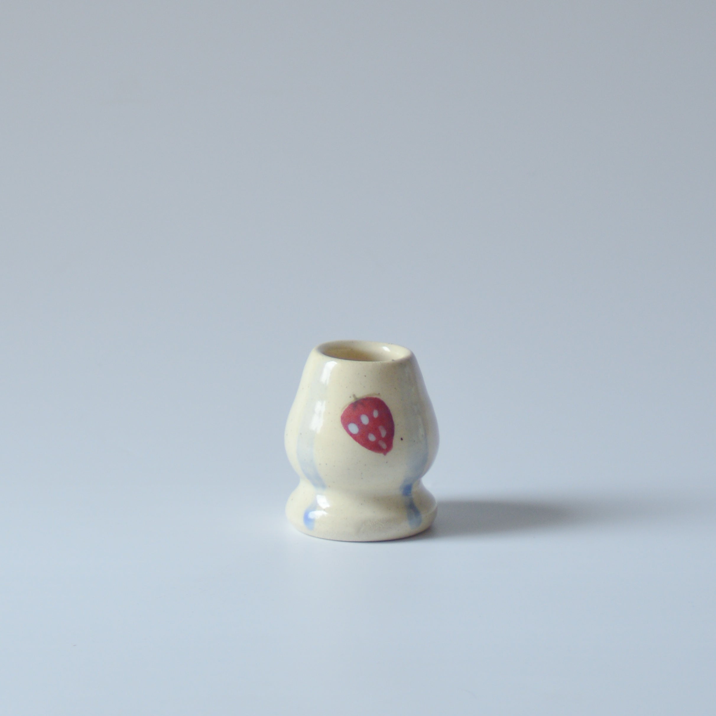 Small ceramic chasen whisk holder with a red strawberry and blue stripes design on a light gray background